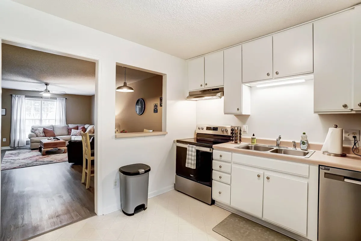 This image displays a welcoming kitchen setup with visible appliances, a sink, and the adjacent dining area. The view captures both the practical workspace for cooking and the inviting table set for meals or work, all bathed in warm, natural light.