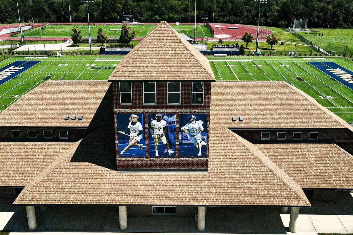 The image features a building with a vibrant mural overlooking a sports field and running track, evoking the campus spirit and the excitement of university sports and community gatherings.