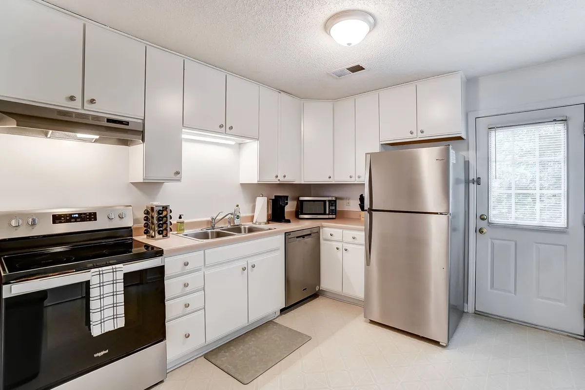 The image features a bright kitchen with stainless steel appliances, ample white cabinetry, and a kitchen sink, providing a clear sense of the cooking essentials available for guests.