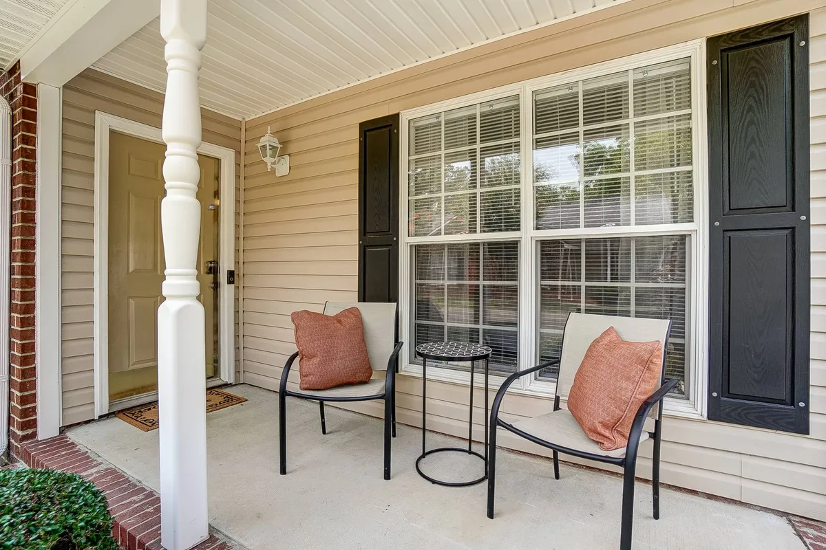 This image shows the inviting front exterior of the property, with a cozy seating area by the front door, colorful decorative pillows, and a small table. The scene suggests a welcoming, homey environment, perfect for relaxing outdoors, sharing stories, or enjoying a morning coffee before heading to campus.