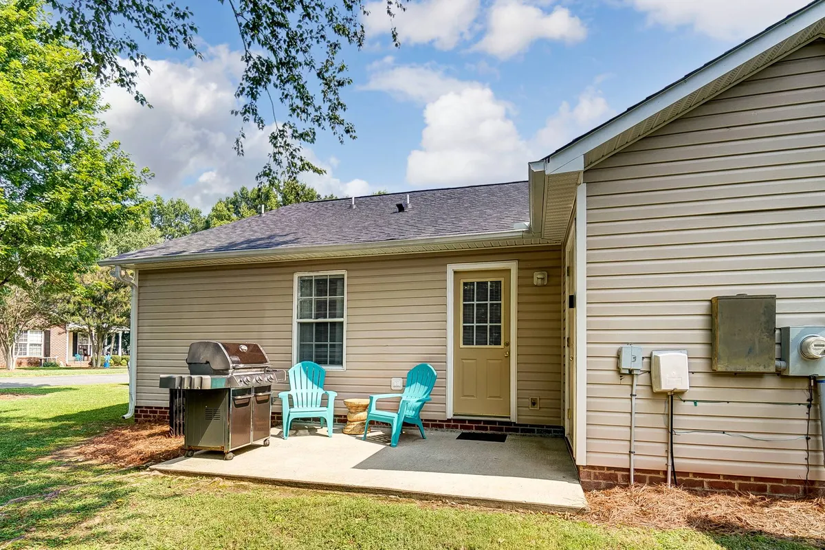 A welcoming exterior patio scene with a grill, blue chairs, and a doorway leading inside. The area is arranged for both barbecuing and relaxation, highlighting the seamless connection between interior comfort and outdoor freedom. The pet-friendly vibe is evident in the casual, inviting setup.