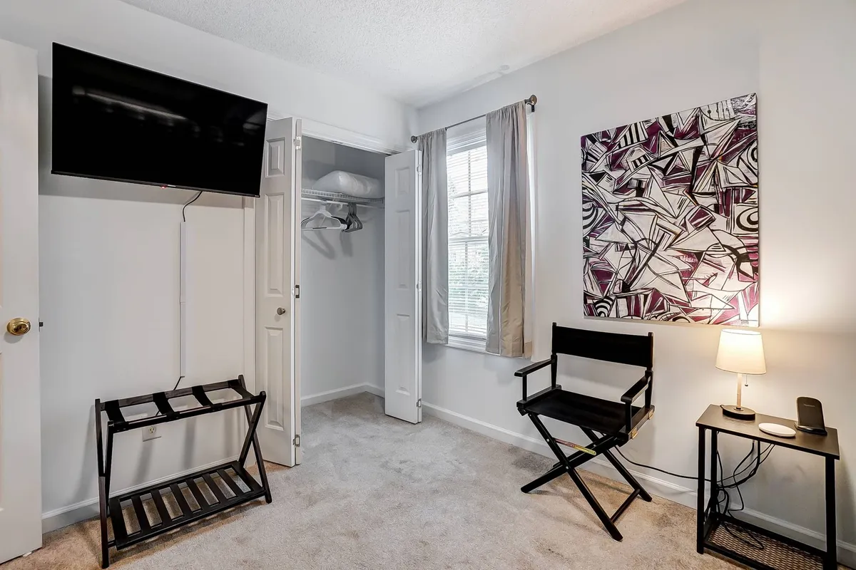 A cozy living area with a television, curated artwork, a comfortable armchair, and natural light filtering through a window, creating an inviting and adaptable space for work, relaxation, or entertainment.