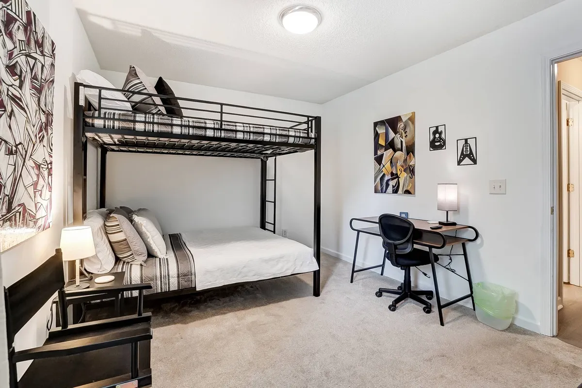 A functional bedroom featuring a bunk bed, a desk with a chair, wall art, and a lamp. The space conveys practicality and warmth, suitable for studying, reading, or shared accommodations, supporting different guest needs.